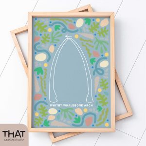 The famous Whitby Whalebone Arch is featured on this design, which sits inside a pale wood frame. The print has a light blue background and seaside pattern of shells and seaweed.